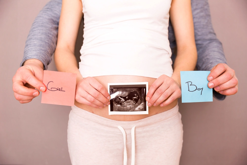 Pregnant woman with her husband holding ultrasound scan and blue and red post its with words boy or girl
